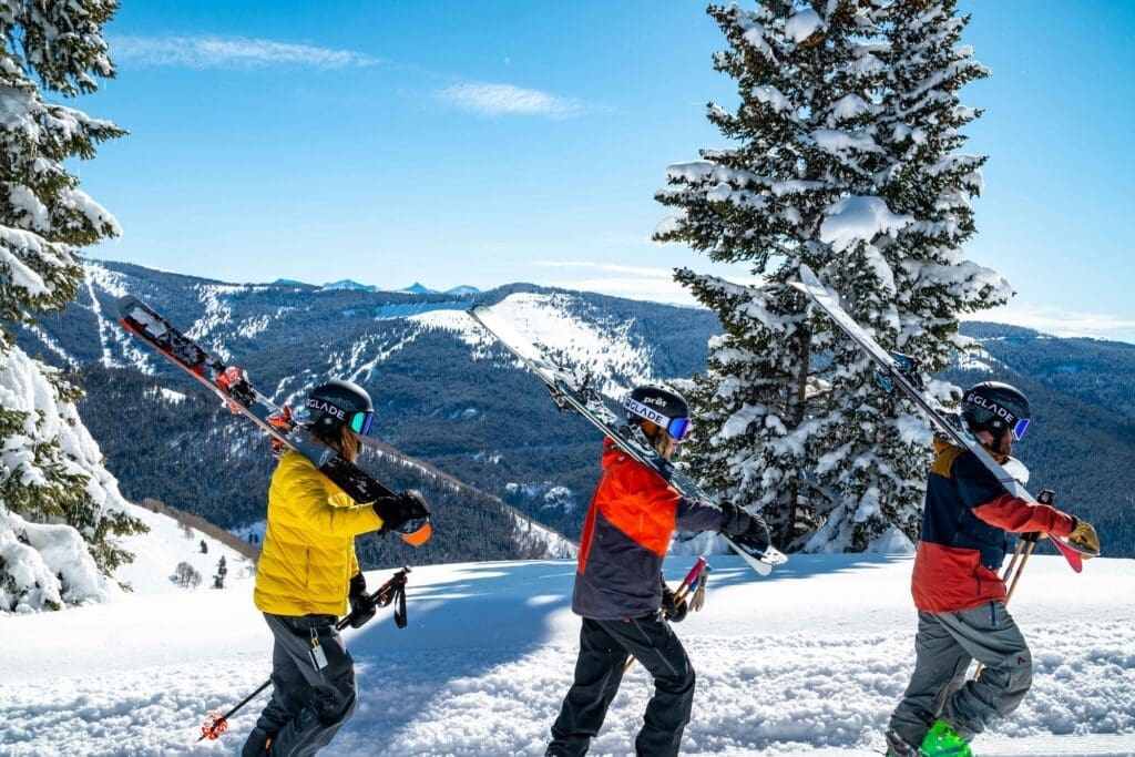 three skiers carrying gear to a new run